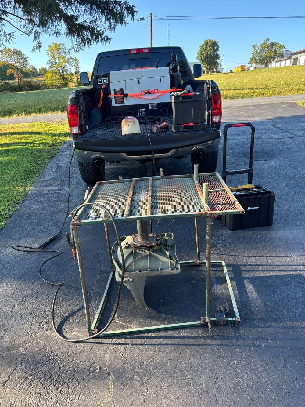 Outdoor workshop setup featuring a workbench, tools, and a truck in the background on a sunny day.