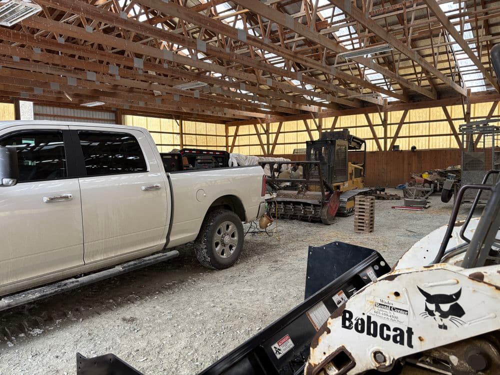 White pickup truck parked inside a spacious barn with various farm equipment.