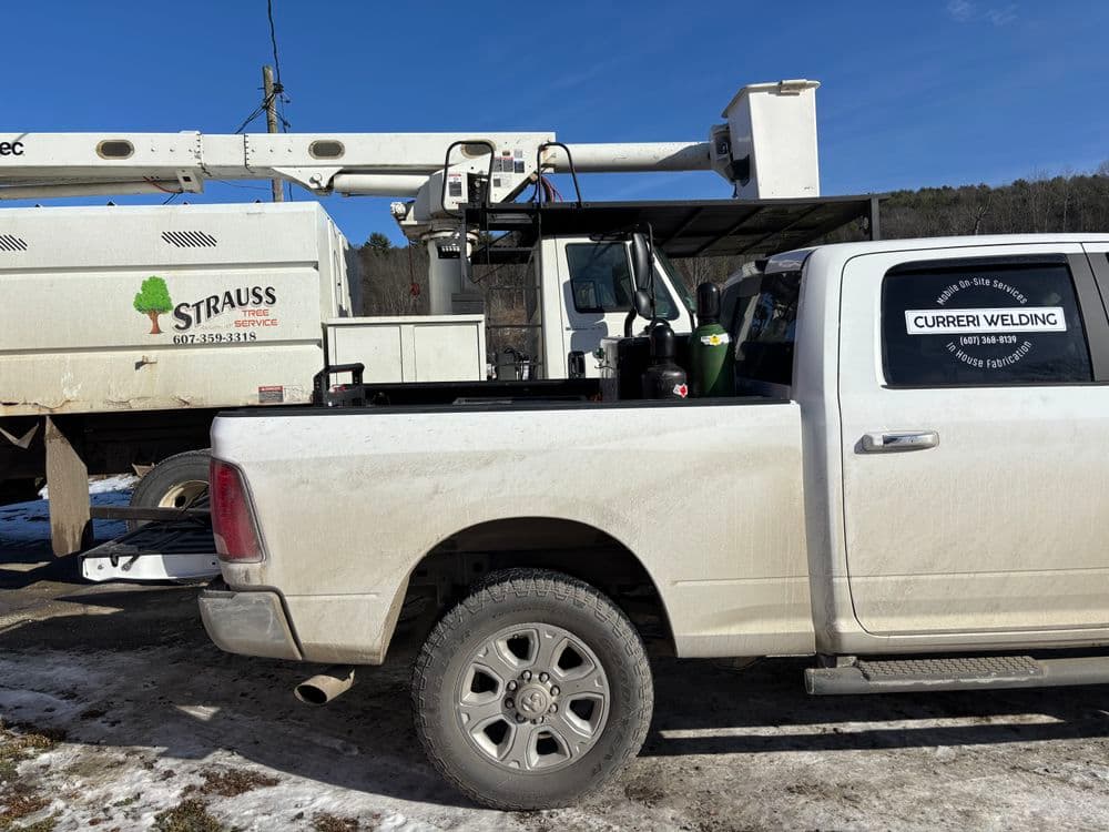 Pickup truck with welding equipment parked near a bucket truck in a rural setting.