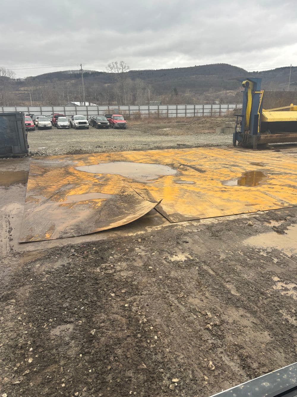 Yellow heavy-duty mat on muddy ground at construction site with cloudy sky and distant vehicles.