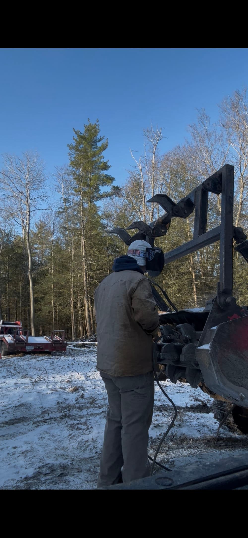 Person operating machinery in a winter forest, surrounded by snow and pine trees.