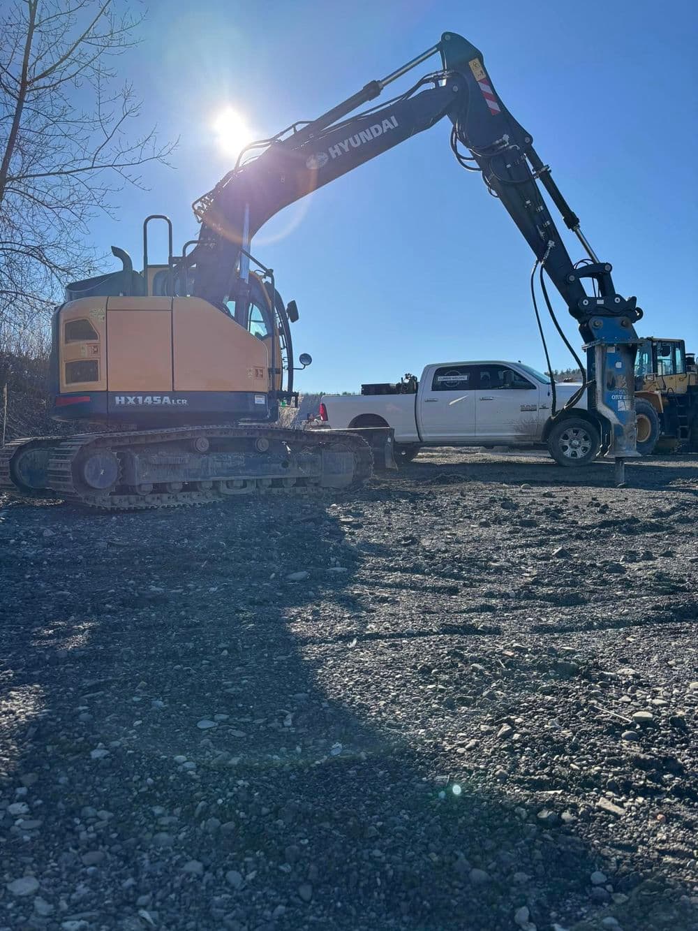 Hyundai HX145AL excavator parked next to a white pickup truck on a construction site.