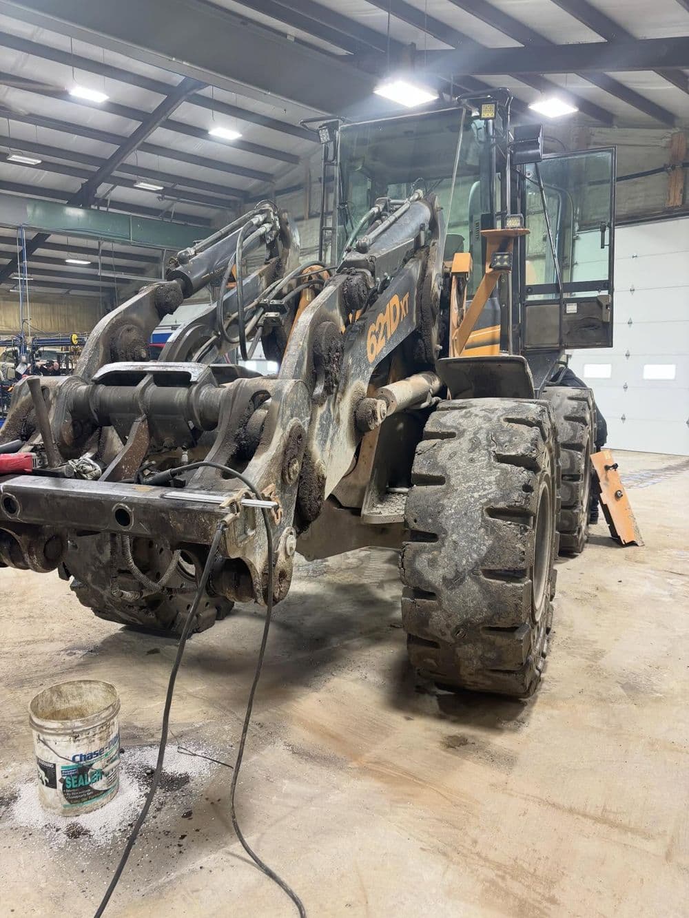 Heavy construction loader in a warehouse with visible wear and tear on tires and equipment.
