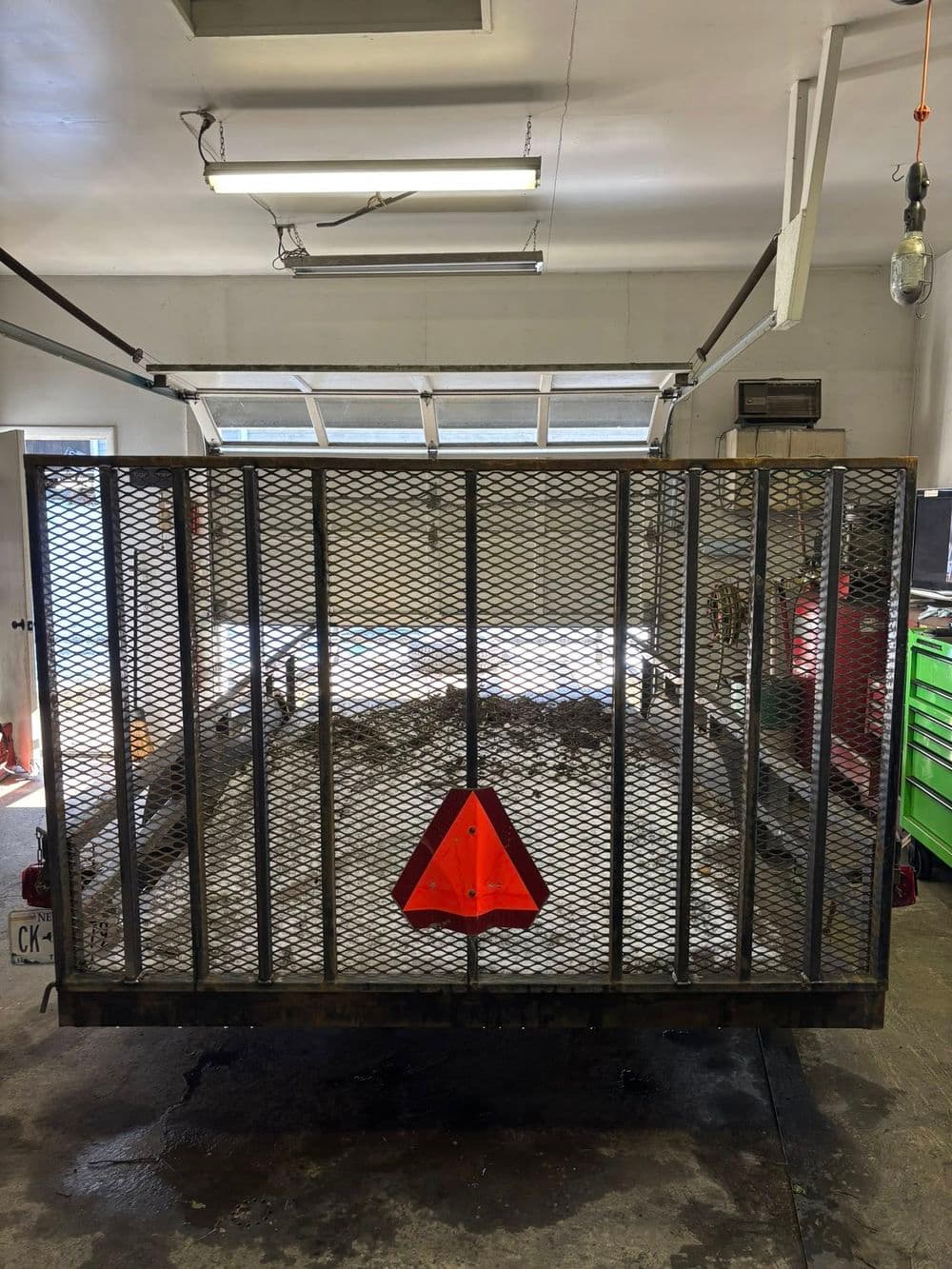 Open trailer with a mesh ramp and a safety triangle, parked in a well-lit garage.
